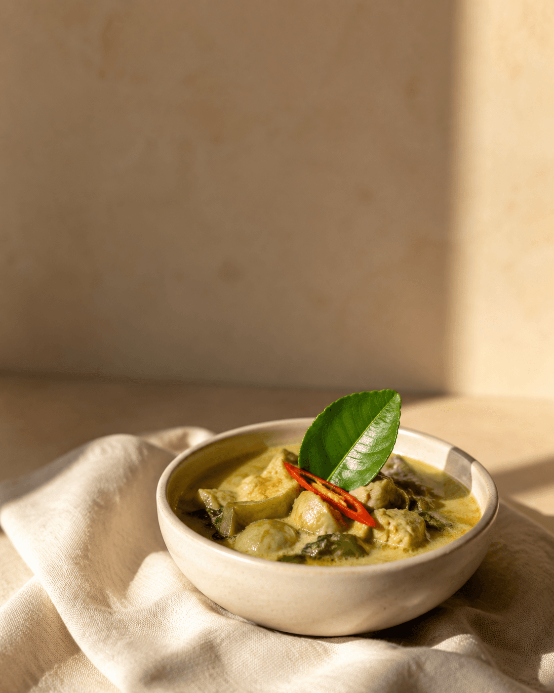 Green curry plated in pale clay bowl with kaffir lime leaf